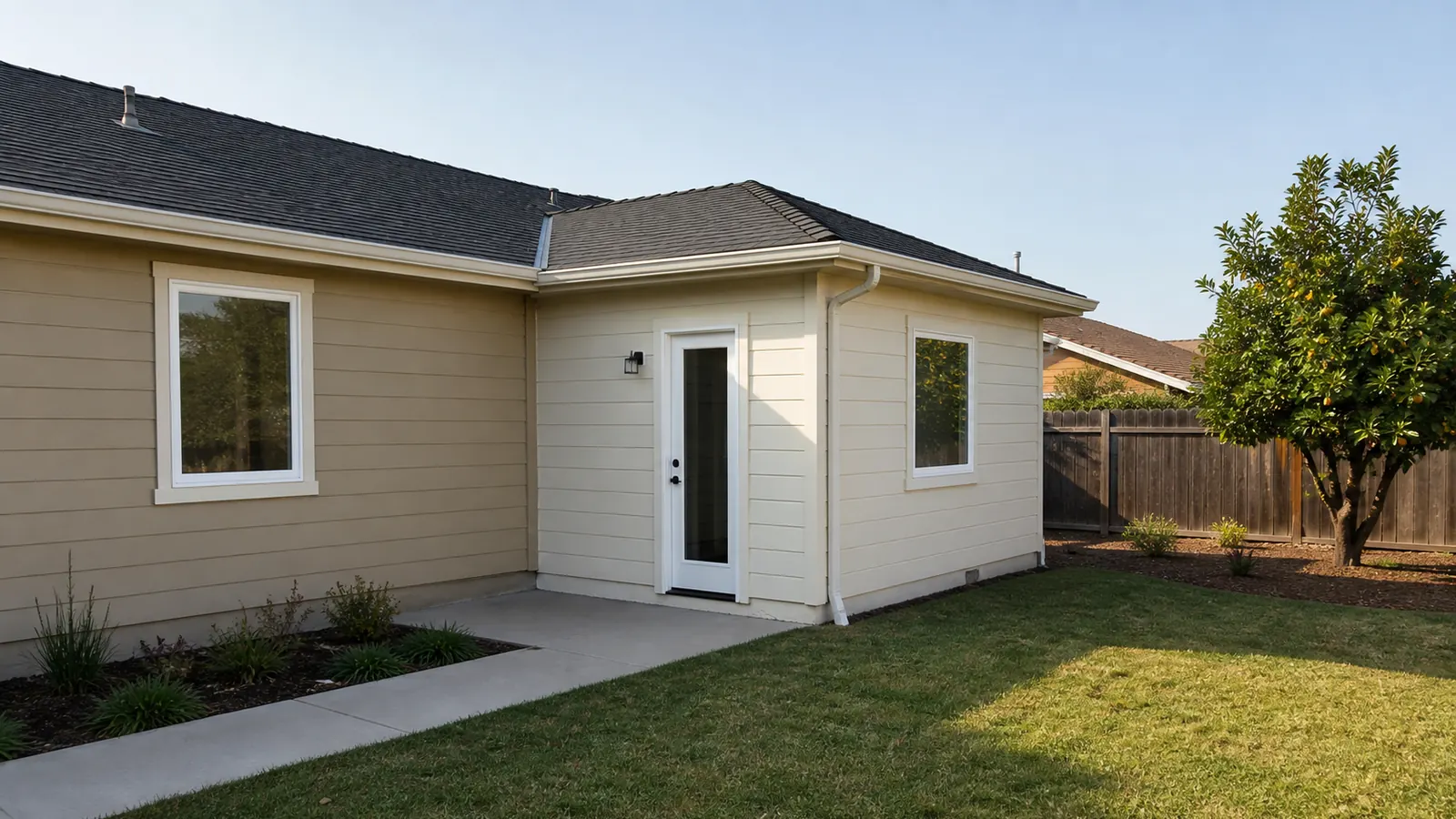 A completed single-story rear addition joined to a modest San Jose ranch house, viewed from the backyard in soft morning light.